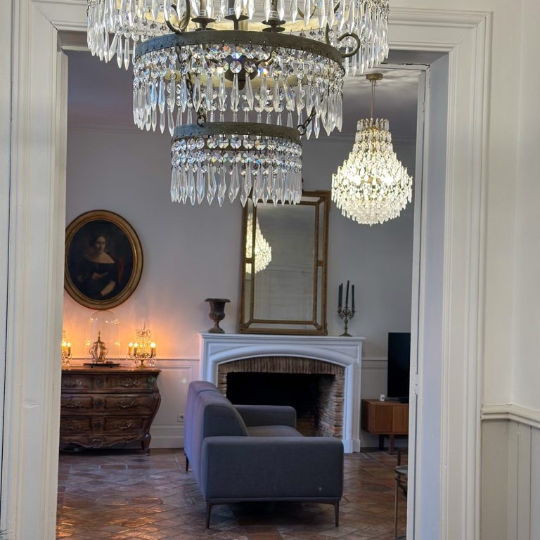Le salon de la demeure Salon de la demeure à Poitiers avec lustre à pampilles, cheminée, miroir et fauteuils.